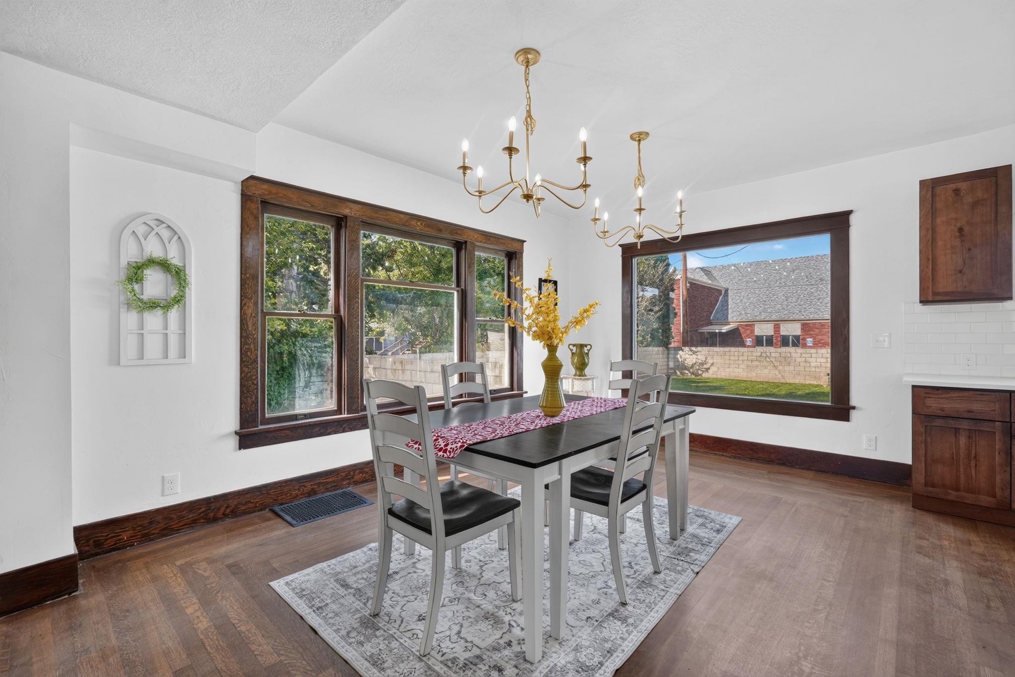 Dining room with dark wood-trimmed windows, a set dining table, and two brass chandeliers.