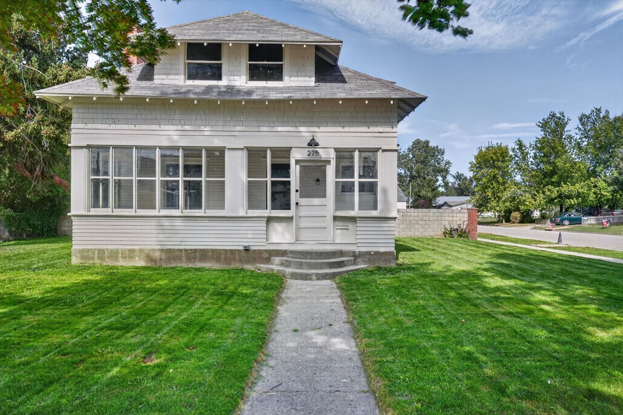 Two-story light-colored house with an enclosed porch and a walkway leading through the lawn to its front door.