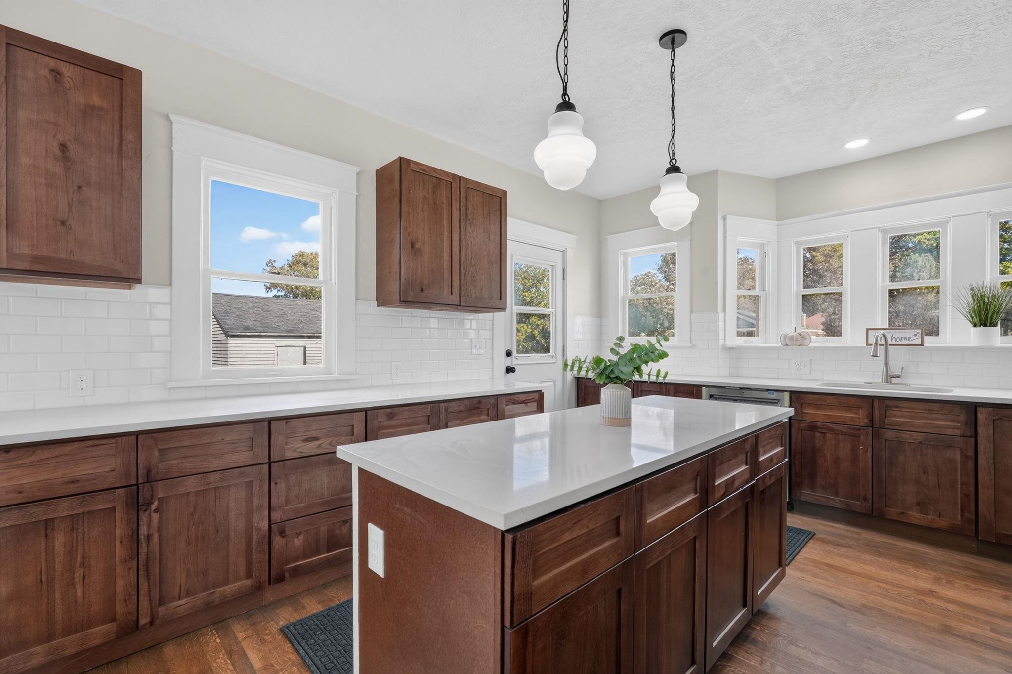 Kitchen with dark wood cabinets, white tile backsplash, and a large island beneath pendant lights.
