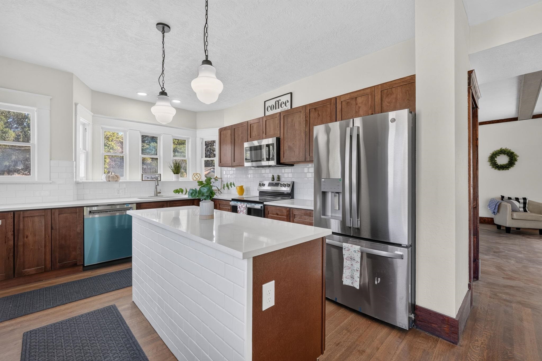 Kitchen with wood cabinets, white tile backsplash, a large island, and stainless steel appliances.
