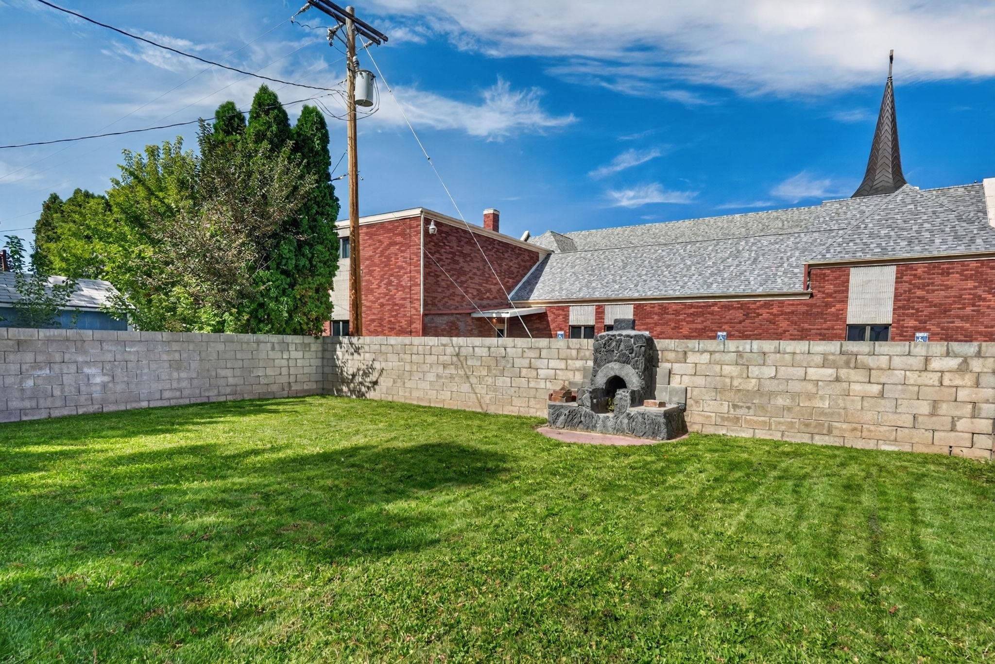 Backyard with a green lawn, stone outdoor fireplace, and block wall.