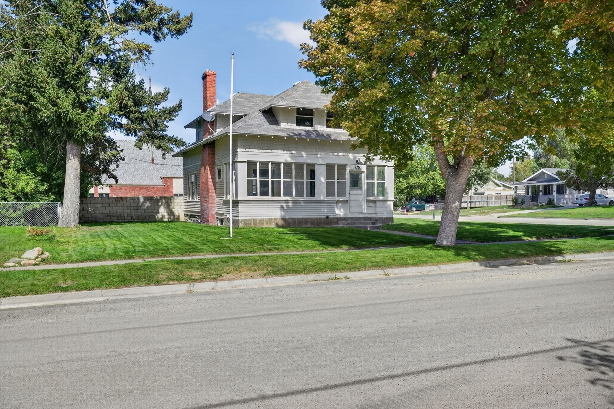 Gray two-story house with an enclosed front porch, red brick chimney, and mature trees.