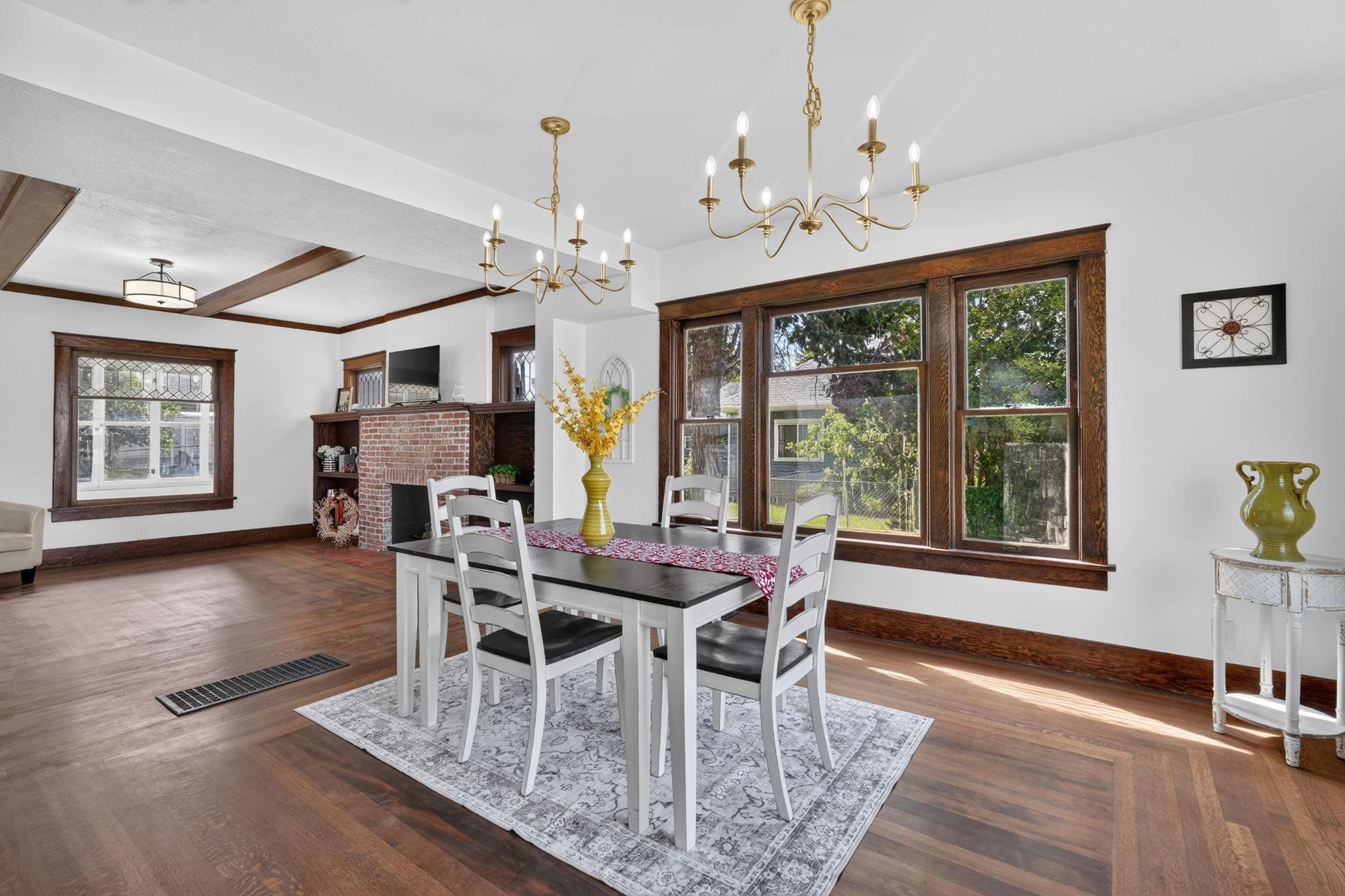Dining room with large wood-trimmed windows, a brick fireplace, and exposed ceiling beams.