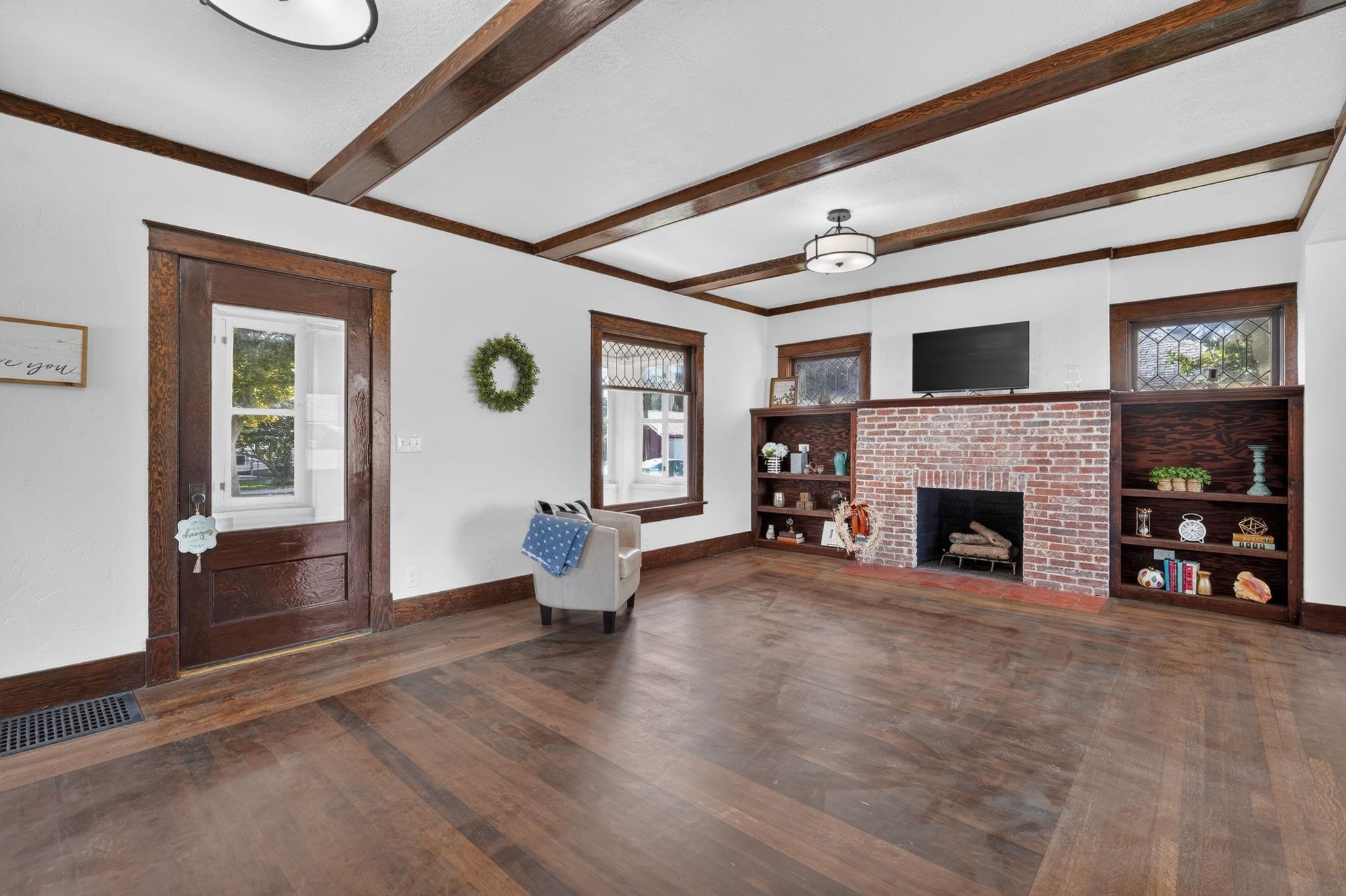 Living room with a brick fireplace, dark built-in shelves, and exposed wood ceiling beams.