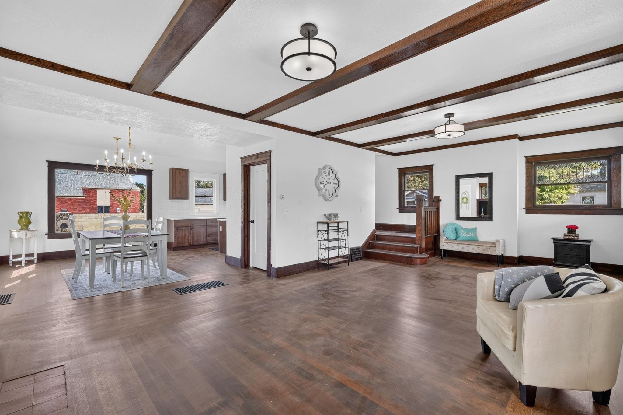 Open living and dining area with exposed wood ceiling beams, a dining set, and stairs.