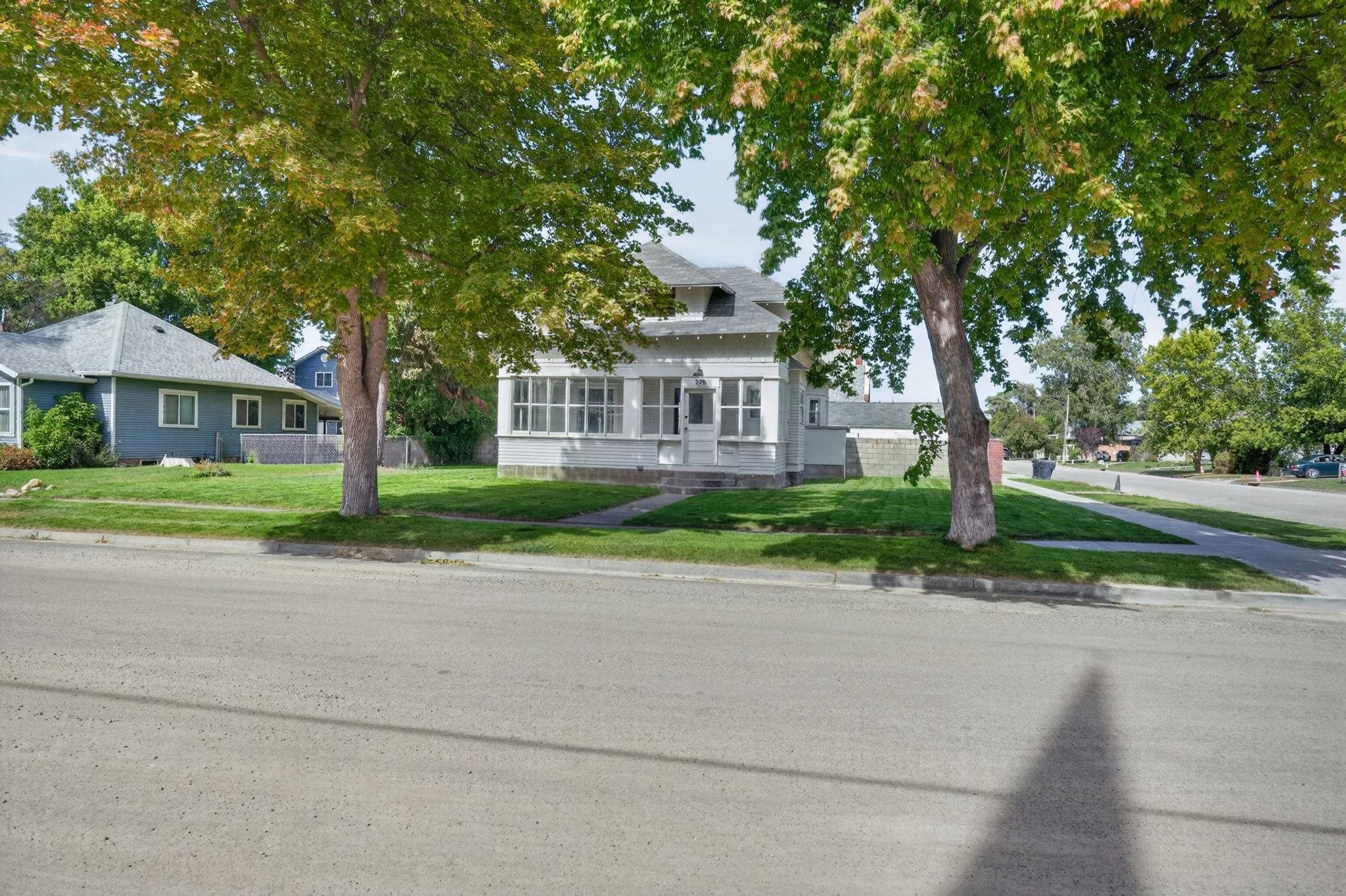 Light-colored house with a covered porch and mature shade trees across the front lawn.