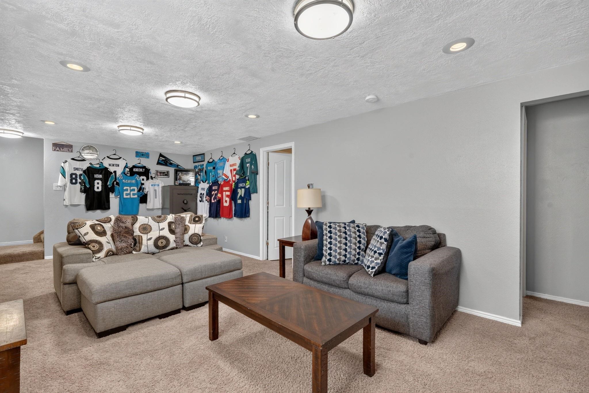Basement family room with gray sofas, a wooden coffee table, and sports jerseys displayed on the wall.