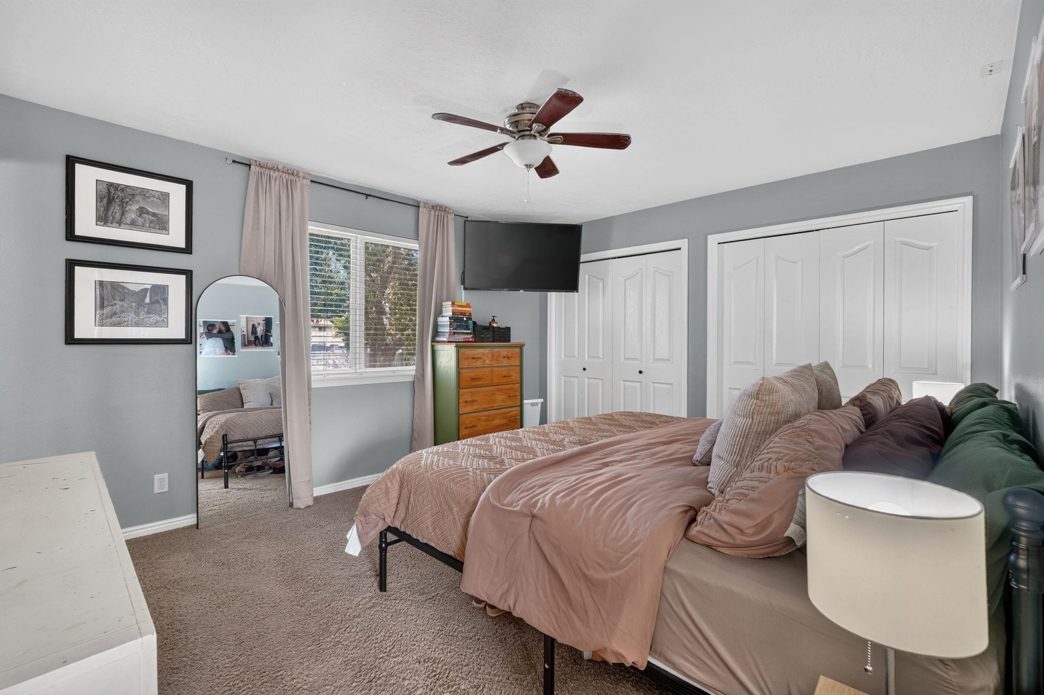 Bedroom with a large bed, white closet doors, and a ceiling fan.