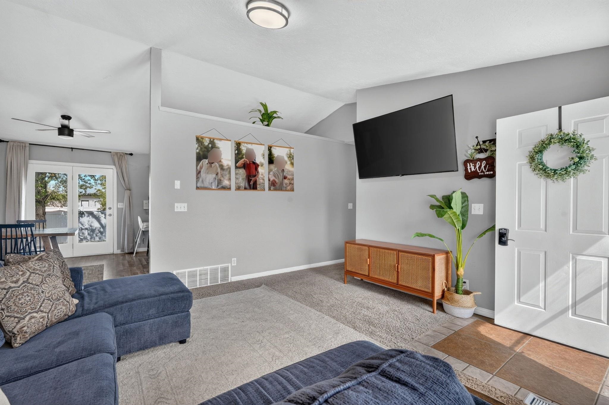 Living room with a blue sectional, wall-mounted TV, and wood media console beside the entry door.