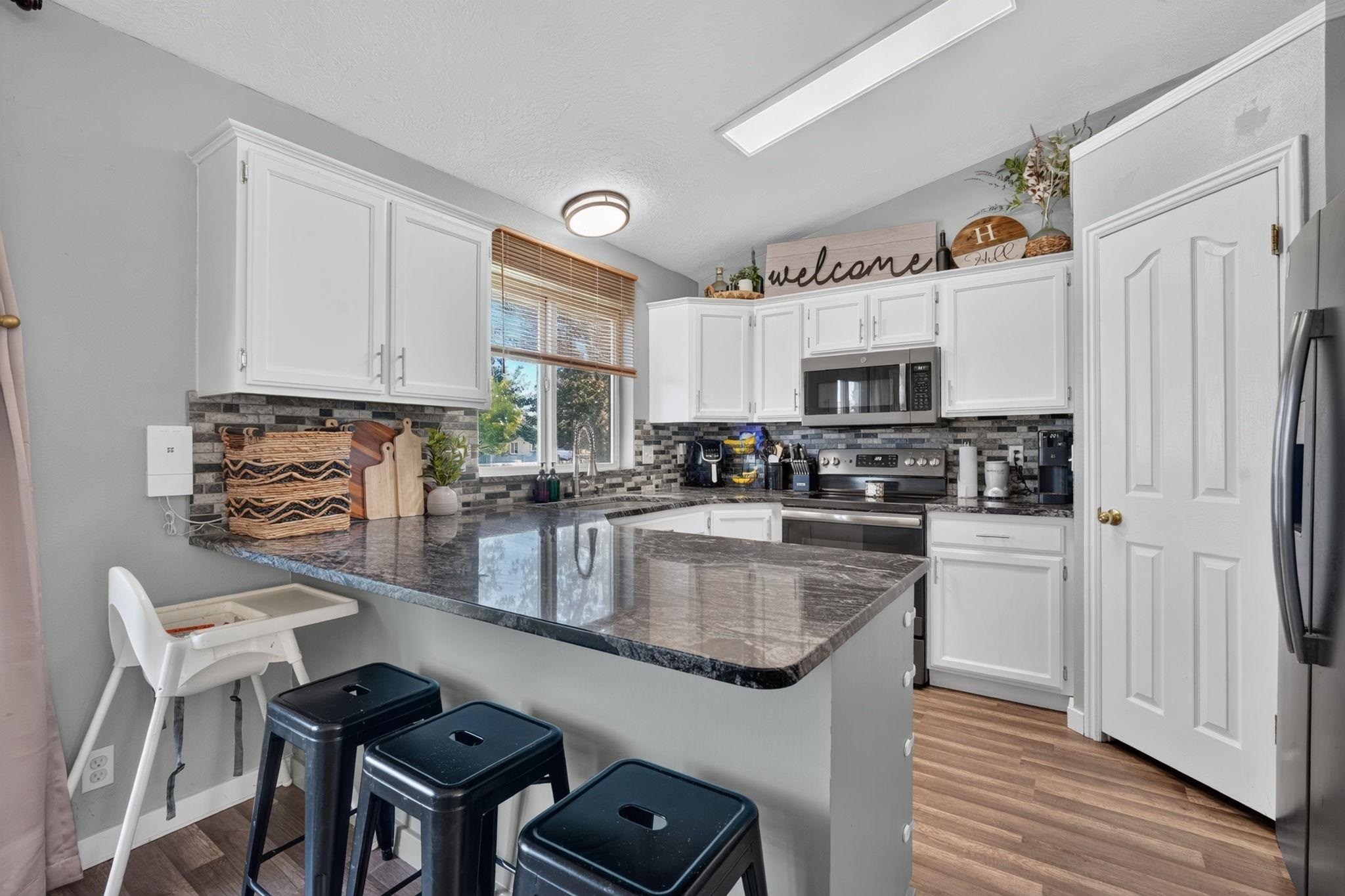 Kitchen with white cabinetry, a granite island, stainless appliances, and dark counter stools.