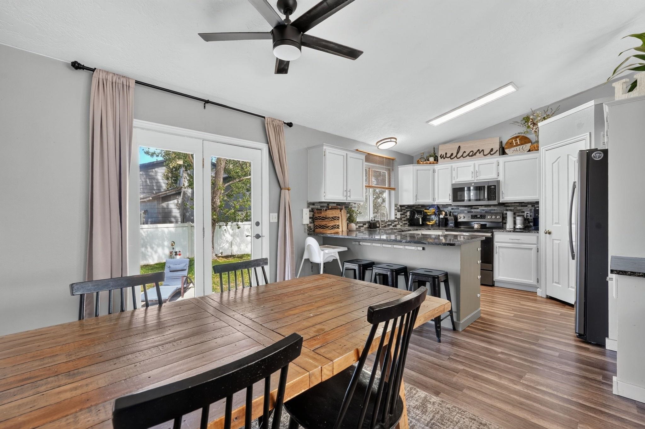 Open kitchen and dining area with white cabinets, a stone island, and a long rustic wood table.