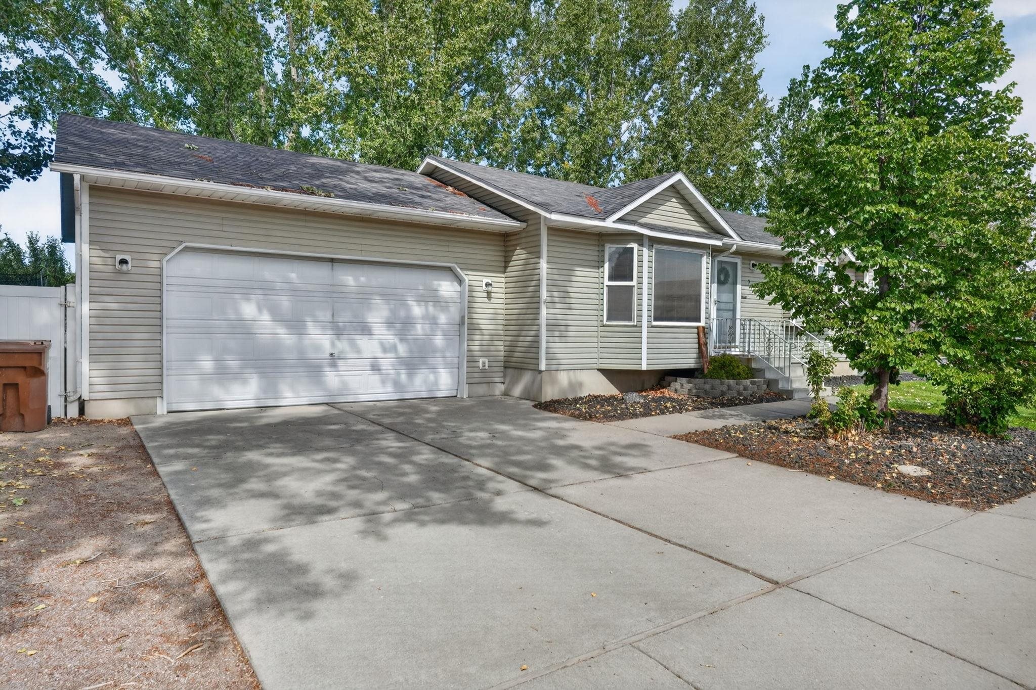 Single-story home with beige siding, a two-car garage, and a wide driveway shaded by mature trees.