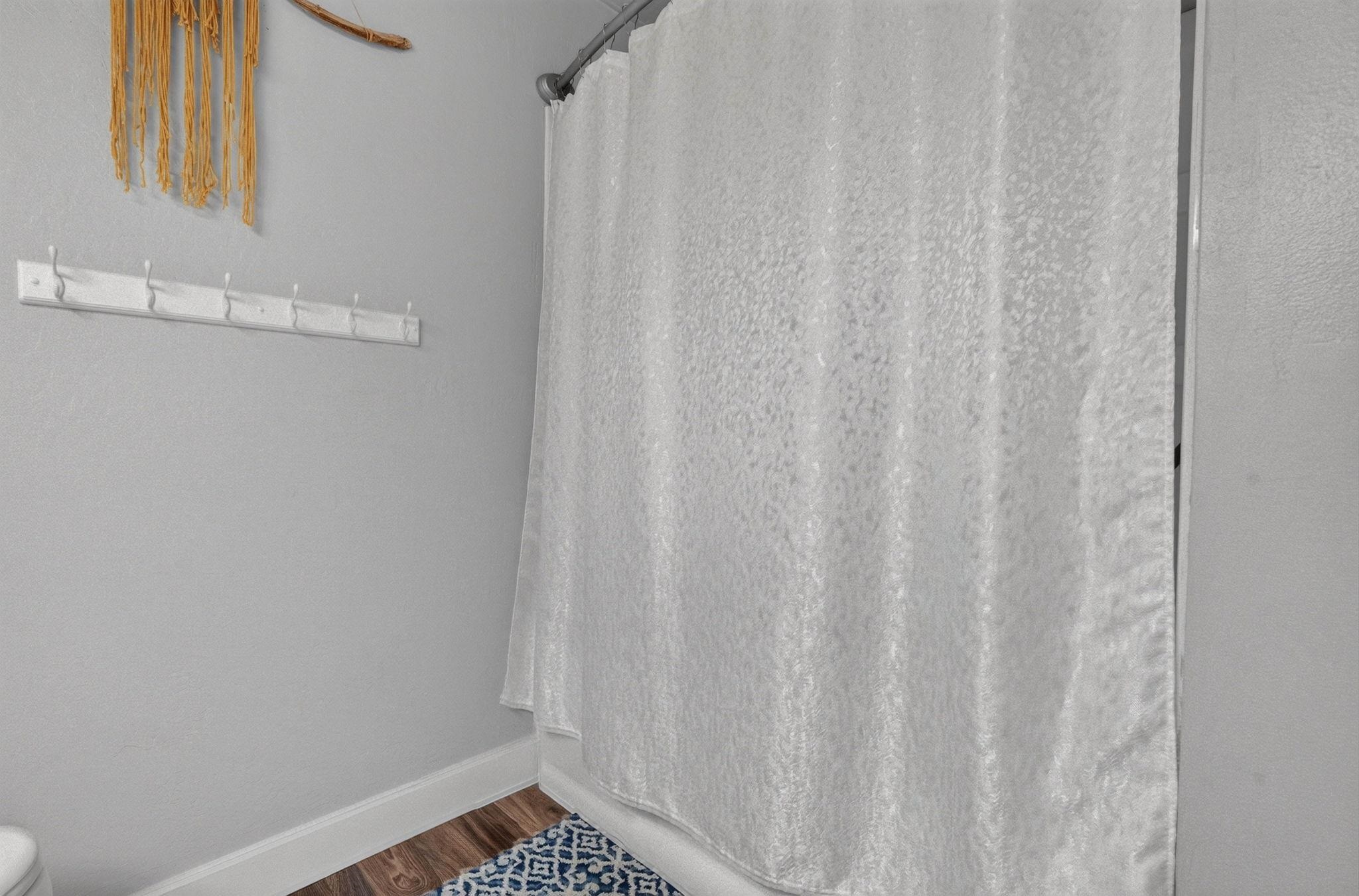 Bathroom with a white patterned shower curtain, wall hooks, and a blue-and-white bath mat.