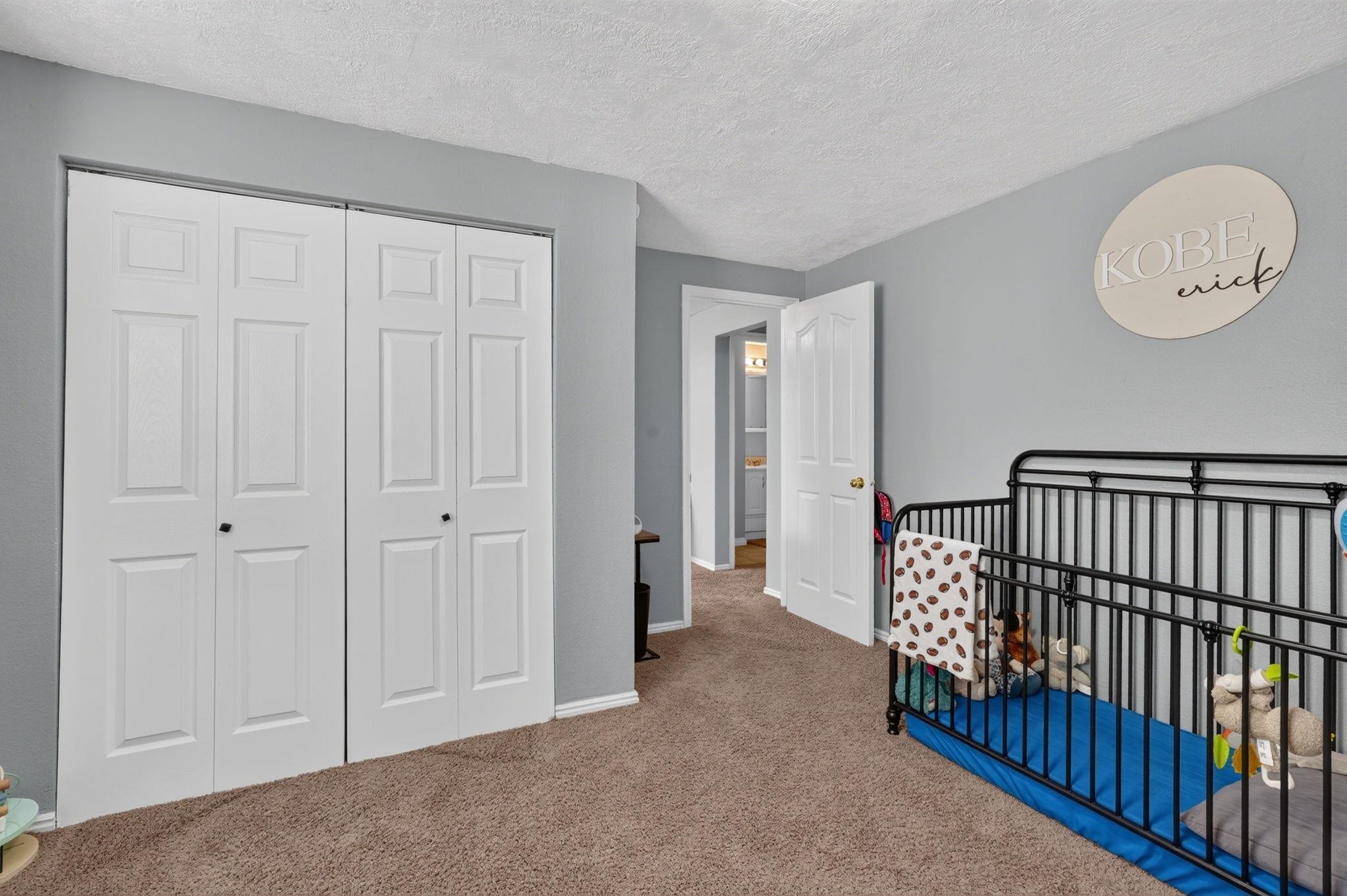 Bedroom with white closet doors and a black metal crib on a blue mattress.