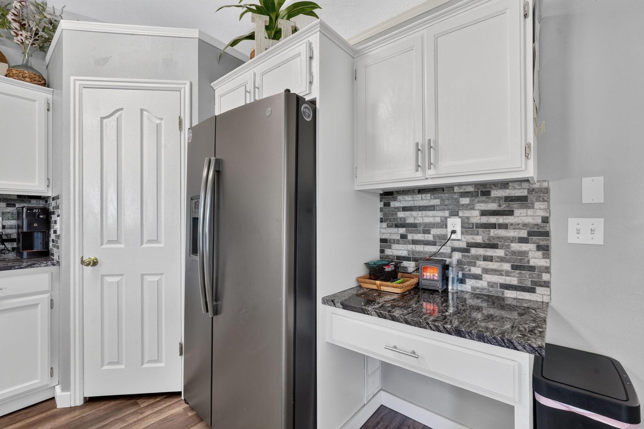 Kitchen with a stainless steel refrigerator, white cabinets, and gray mosaic tile backsplash.