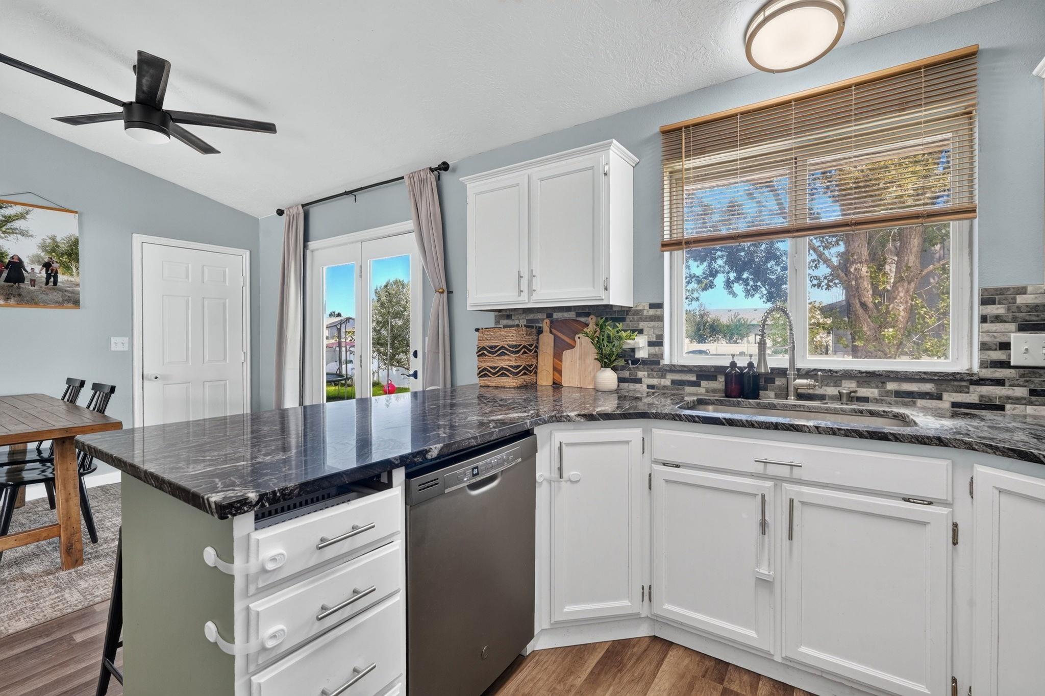 Kitchen with white cabinets, dark countertops, a tiled backsplash, and a large window over the sink.