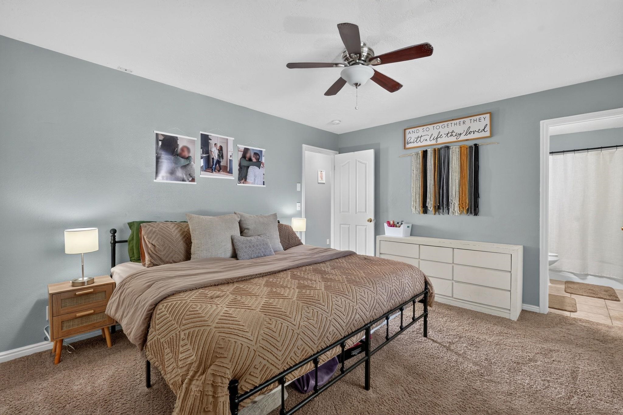 Bedroom with a black metal bed, patterned tan bedding, and an open doorway to a bathroom.
