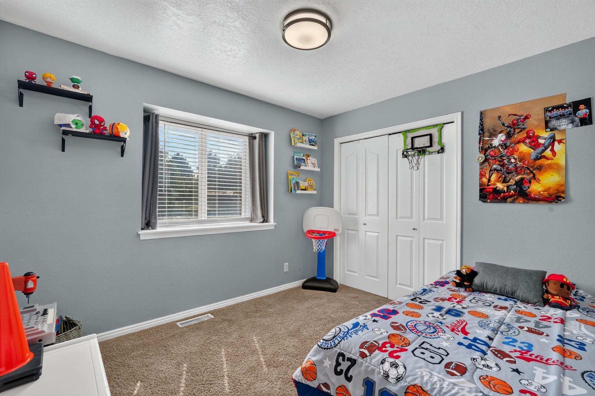 Child’s bedroom with a sports-themed bed, superhero decor, and a small basketball hoop on the closet doors.