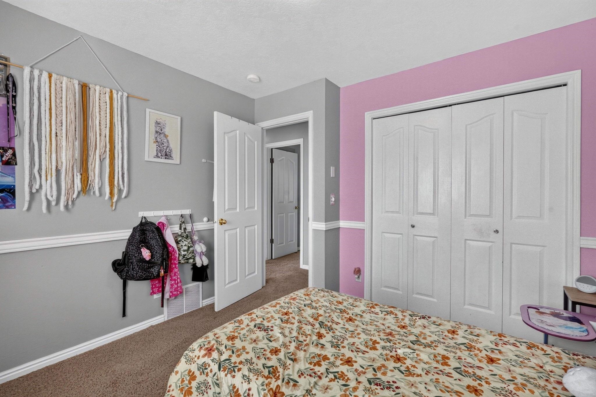 Bedroom with pink accent wall, white closet doors, and a floral bedspread.