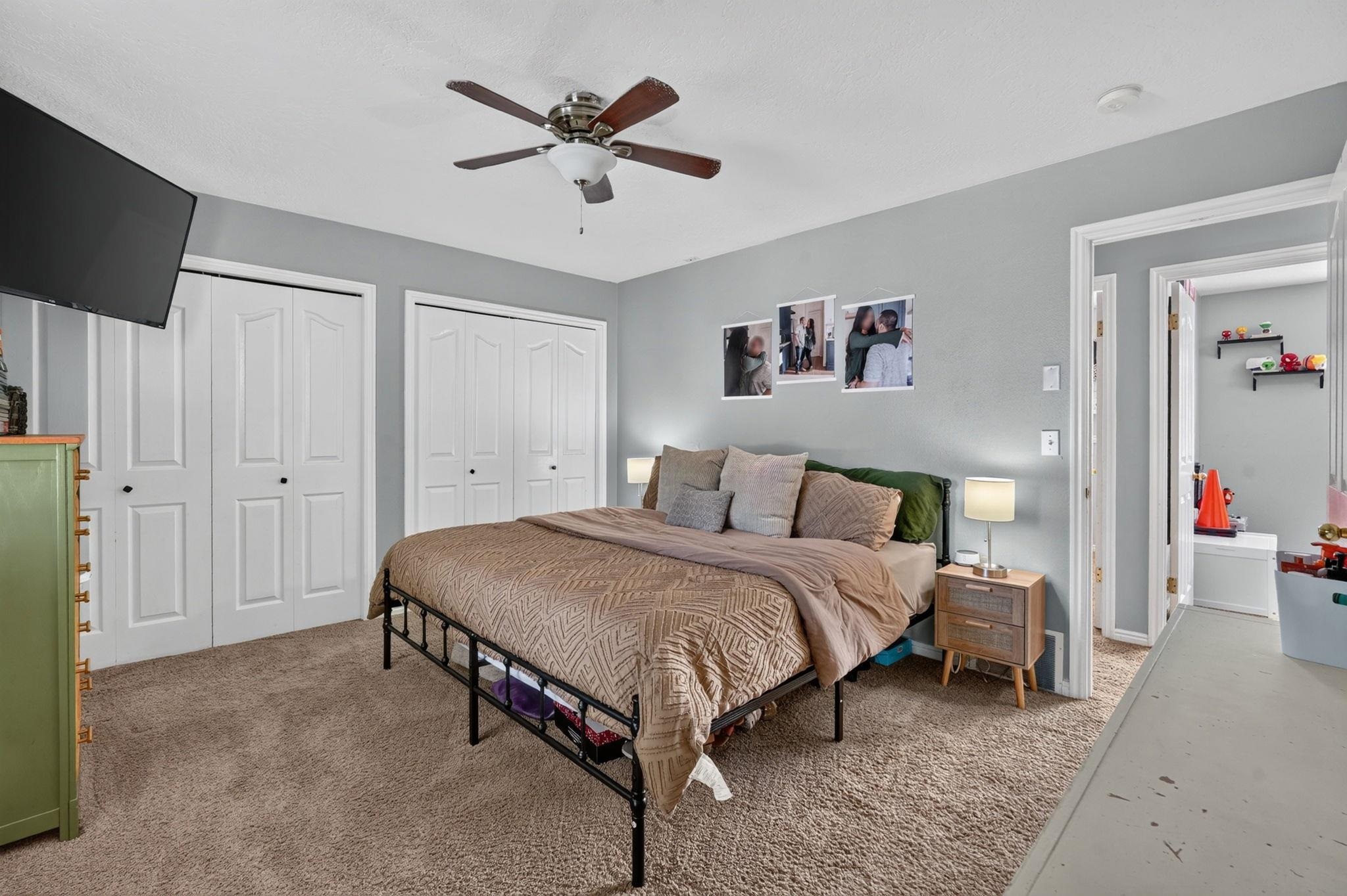 Bedroom with a black metal bed, patterned taupe bedding, and white closet doors.