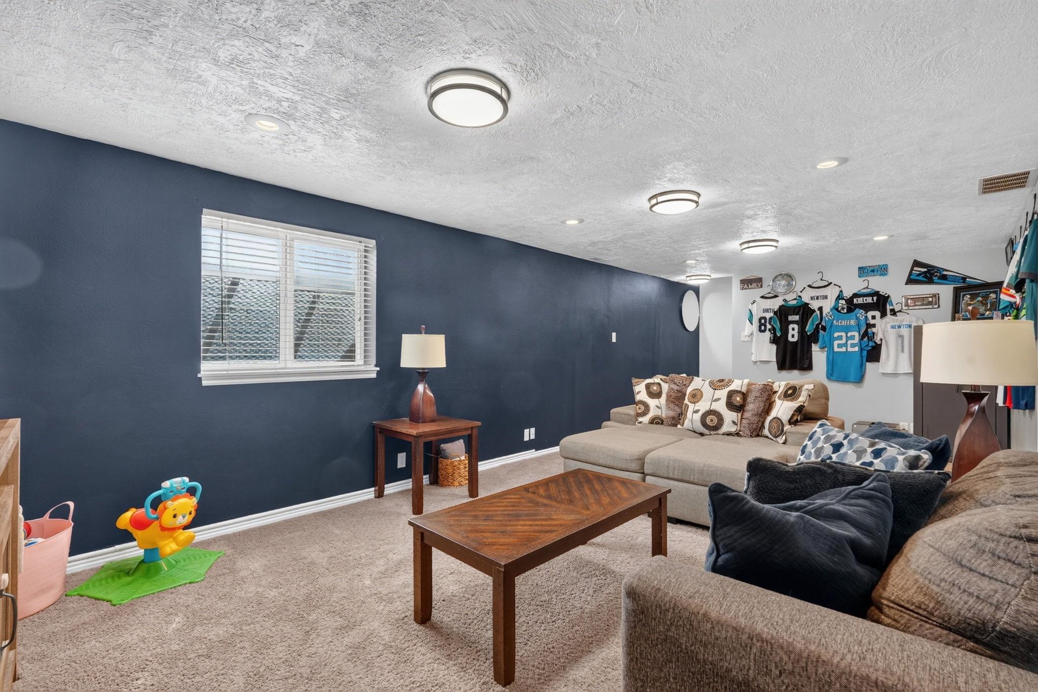 Furnished living room with navy walls, a sectional sofa, and sports jerseys displayed on the far wall.
