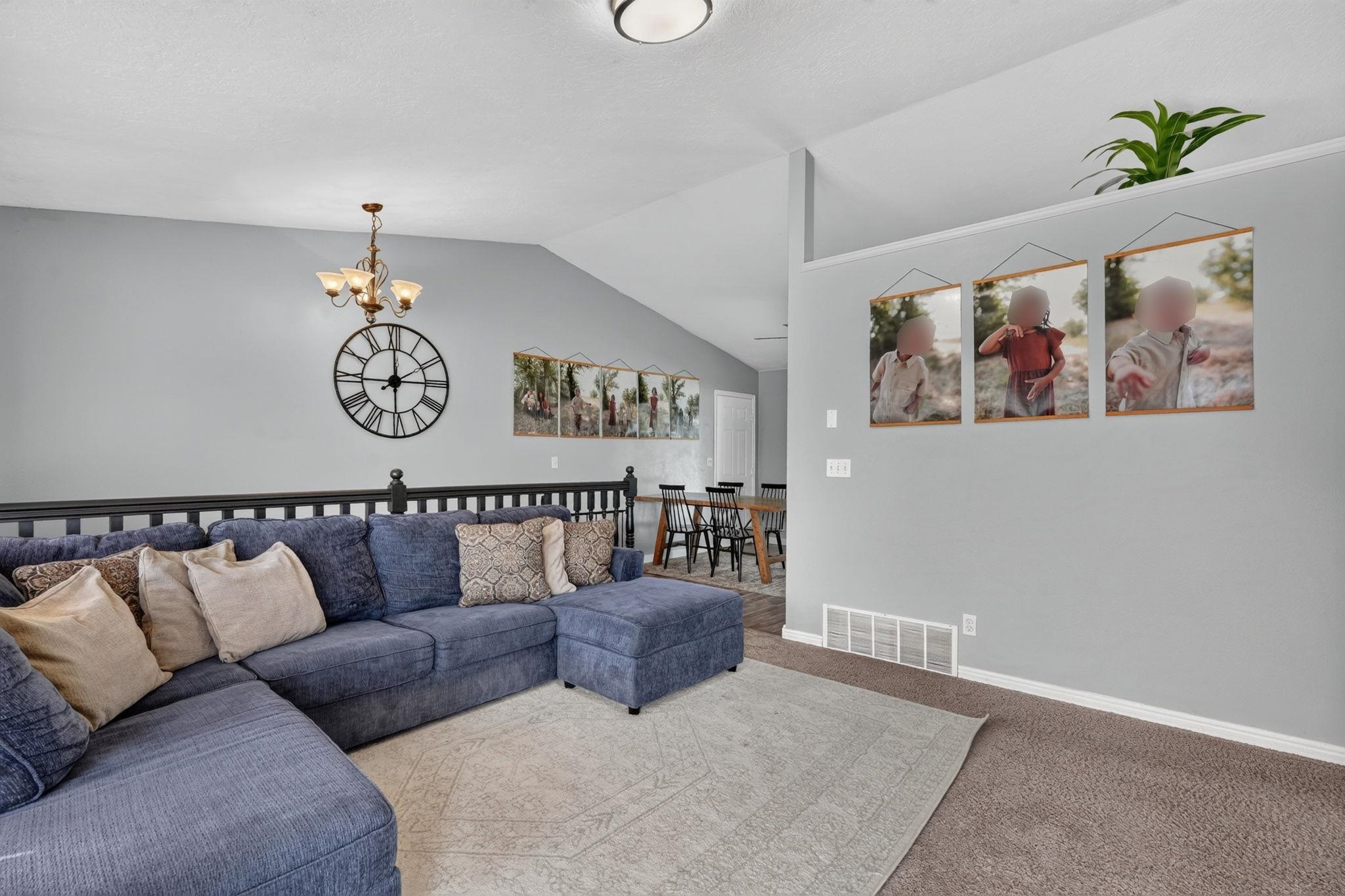 Living room with a blue sectional, vaulted ceiling, oversized clock, and dining area beyond.