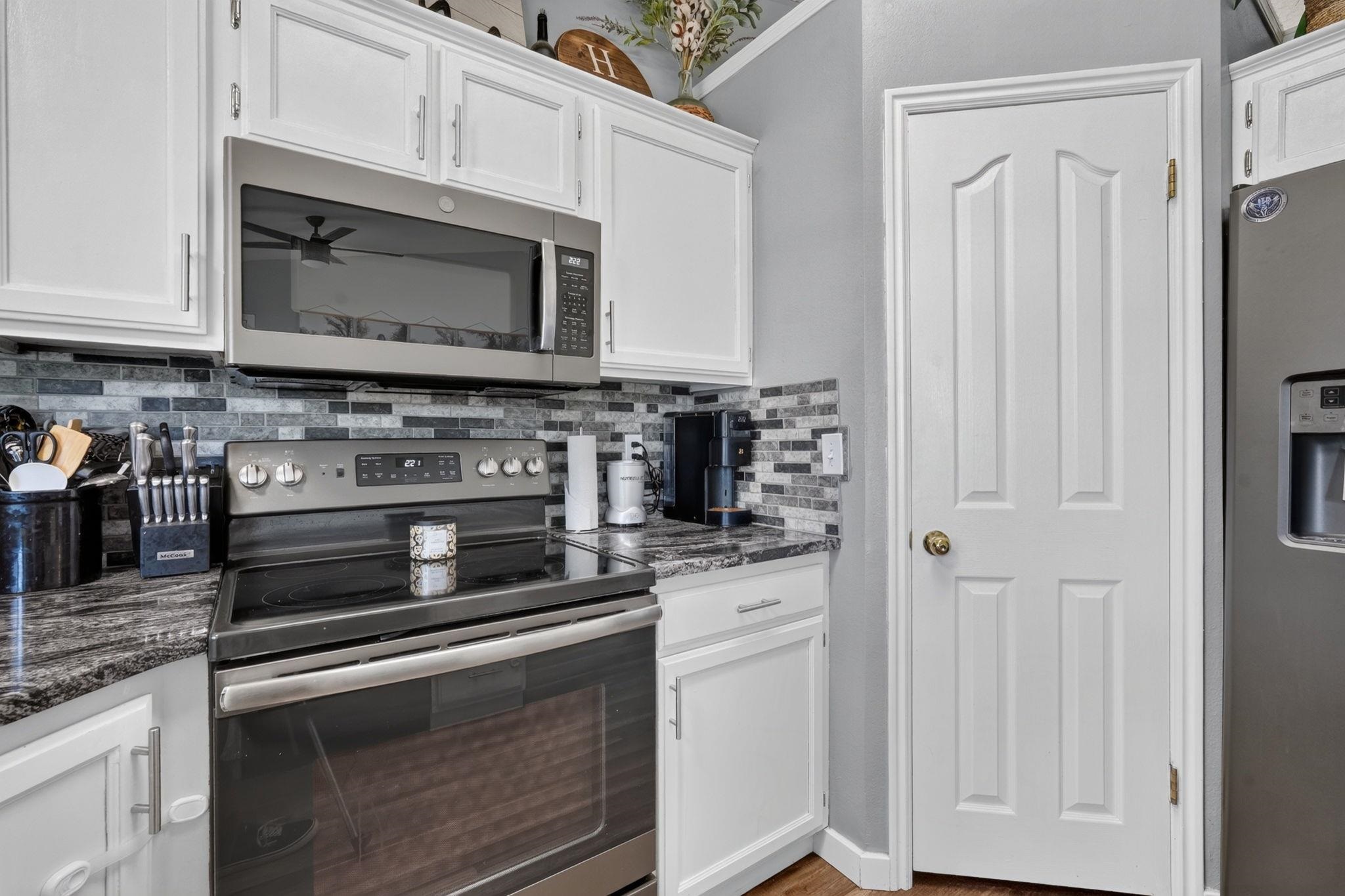 Kitchen with white cabinets, stainless steel appliances, dark stone counters, and a gray mosaic backsplash.