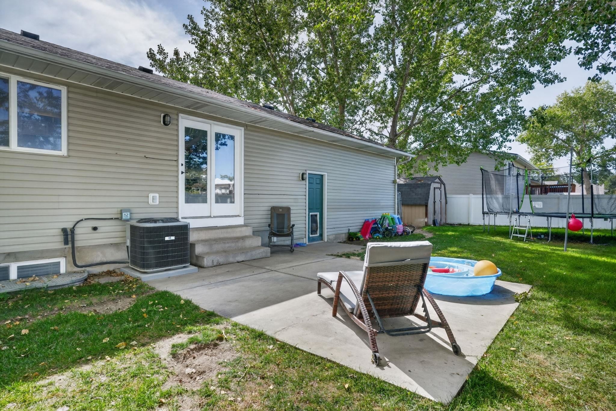Backyard patio with sliding doors, lounge chairs, a wading pool, and a fenced lawn with a trampoline.