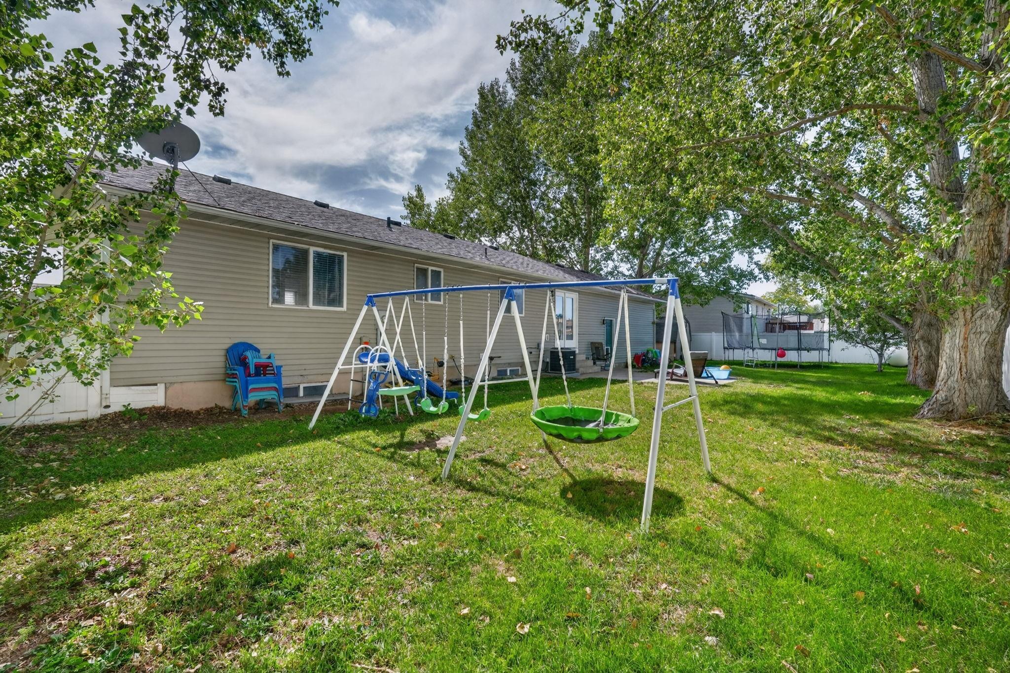 Home backyard with a large swing set, spacious lawn, and mature shade trees.