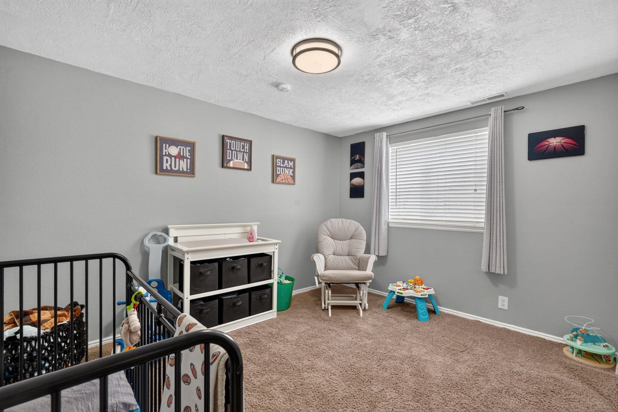 Nursery with a black crib, white storage shelf, rocking chair, toys, and sports-themed wall art.