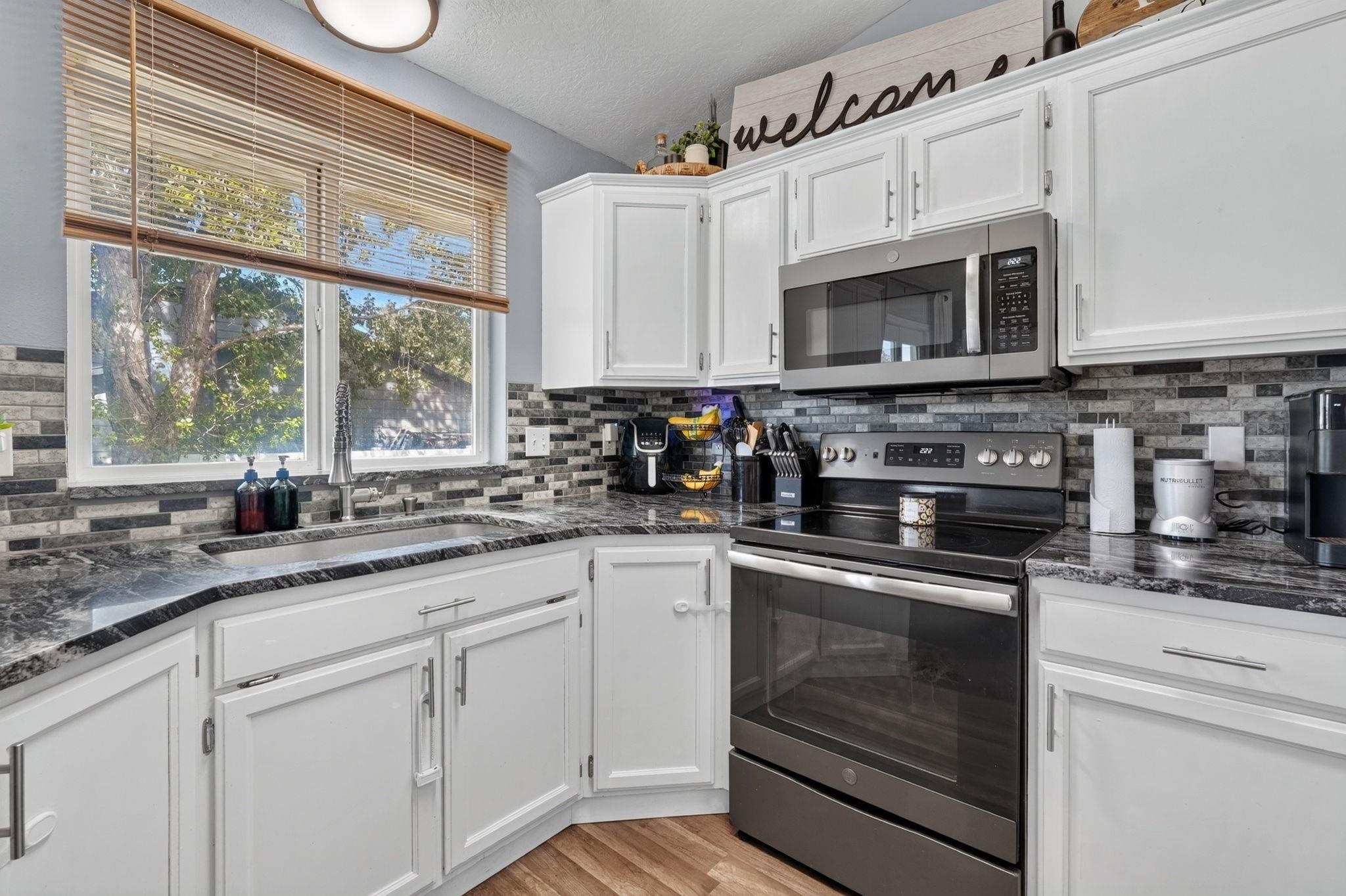 Kitchen with white cabinets, dark stone counters, gray tile backsplash, and stainless steel appliances.
