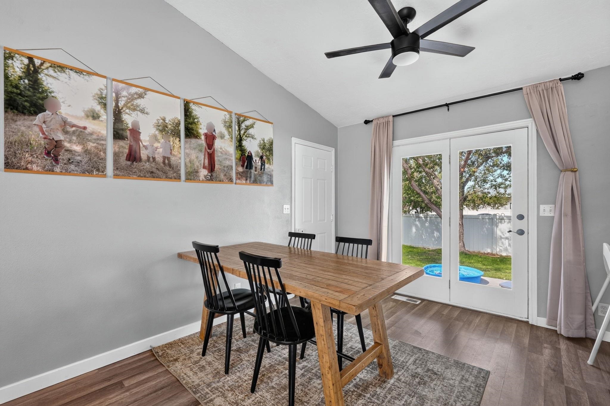 Dining area with a rustic wooden table, black chairs, and glass doors to a fenced backyard.