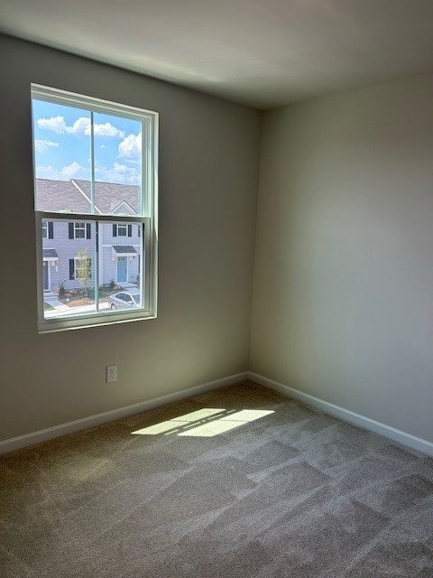 Empty carpeted room with beige walls, a window, and sunlight across the floor.