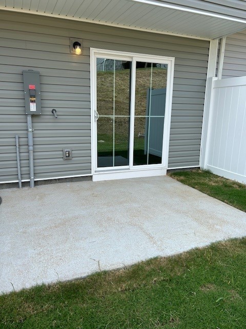 Covered concrete patio outside a home, with sliding glass doors and a small lawn.