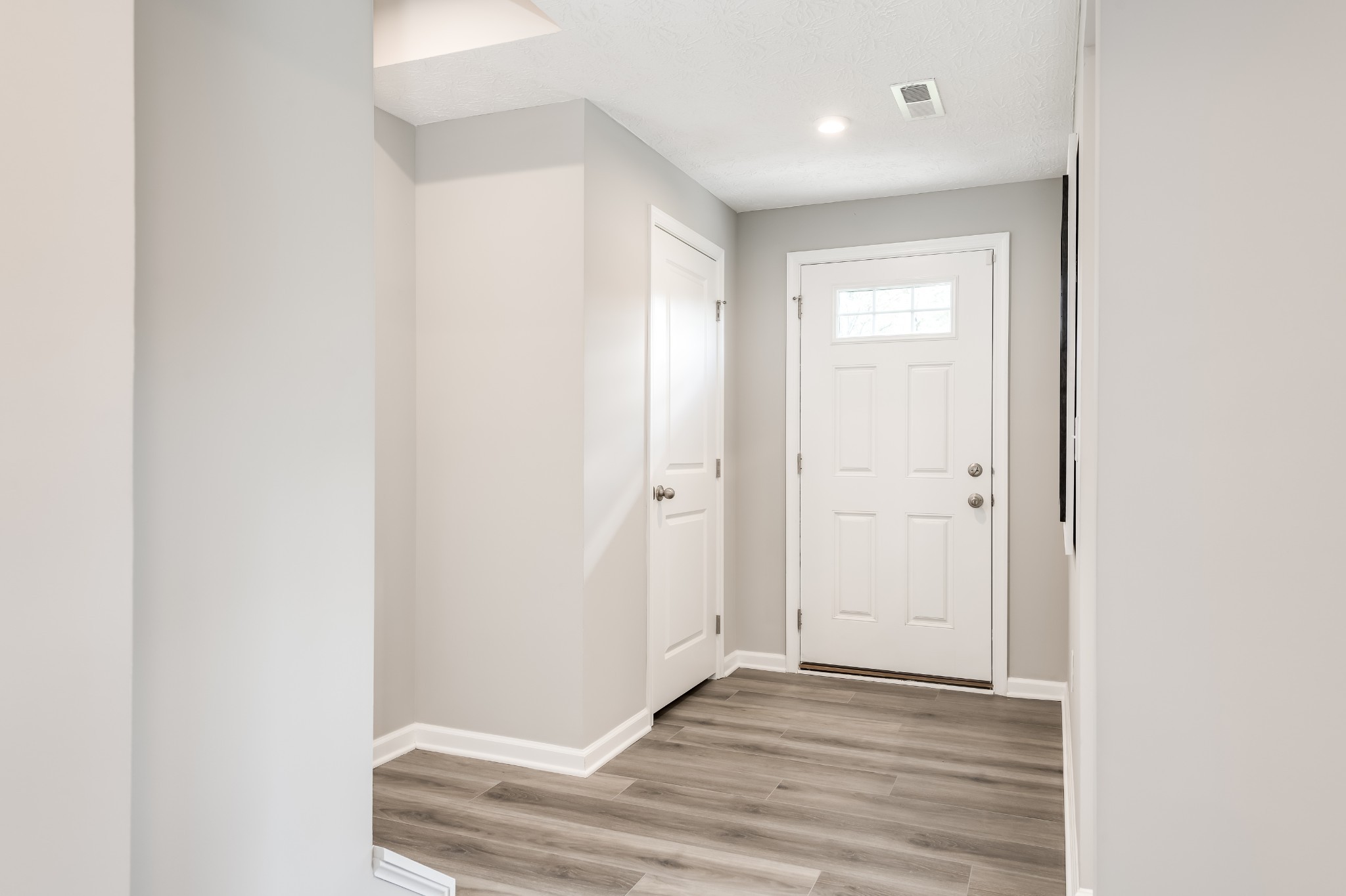 Entryway with gray wood-look flooring and a white front door with a small window.