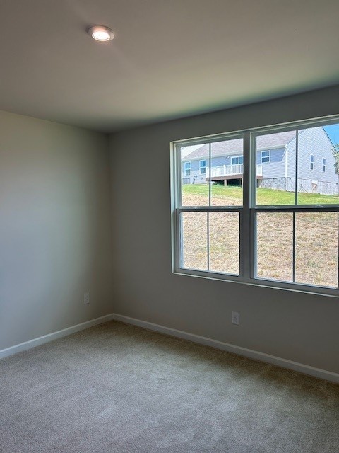 Empty carpeted bedroom with a large window overlooking neighboring homes.