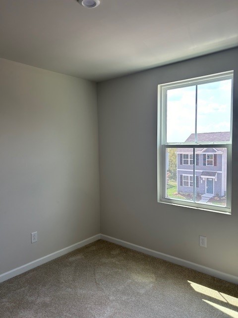 Empty carpeted room with gray walls and a window overlooking a neighboring townhouse.