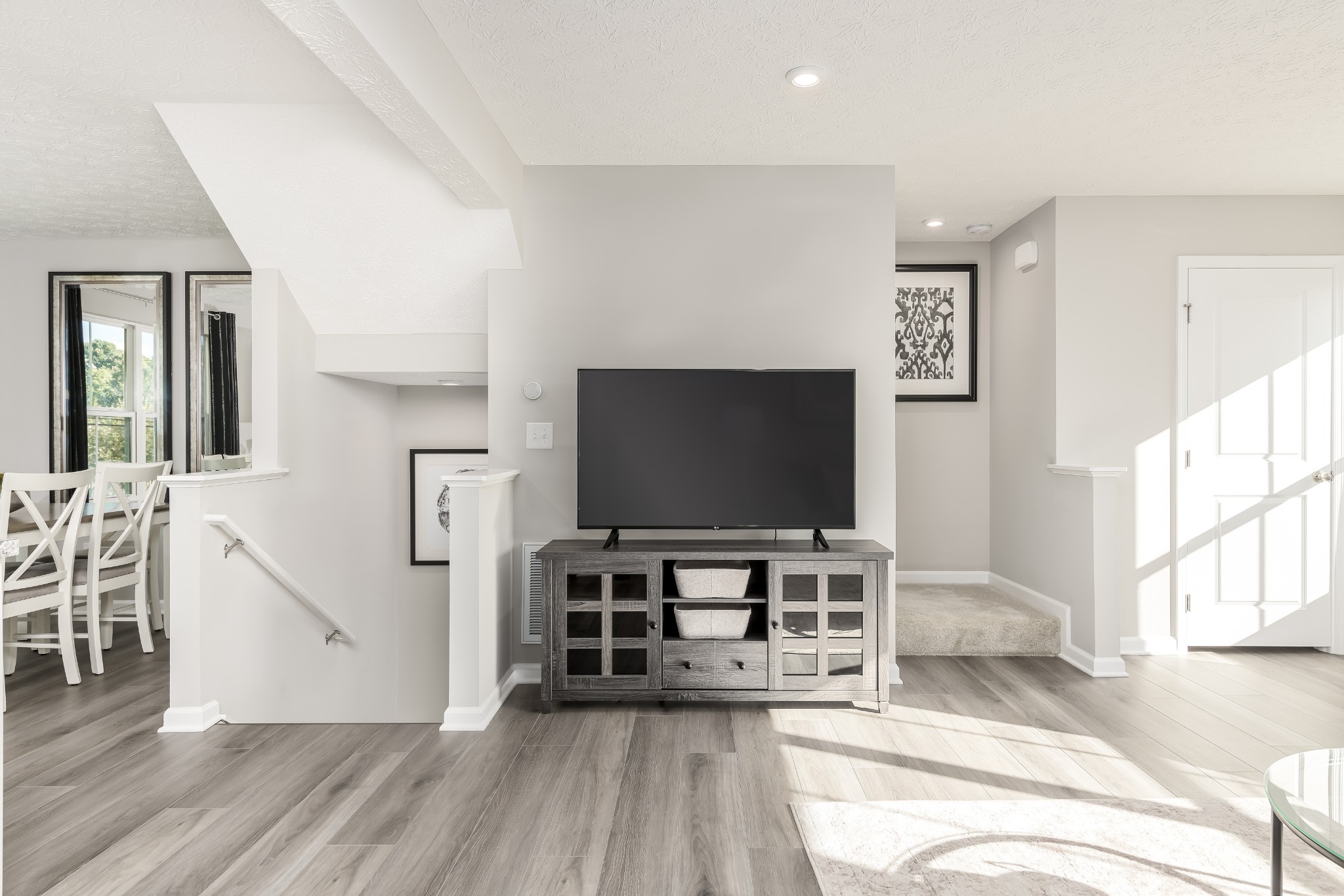Furnished living room with a large TV, gray media cabinet, and staircase beside the dining area.
