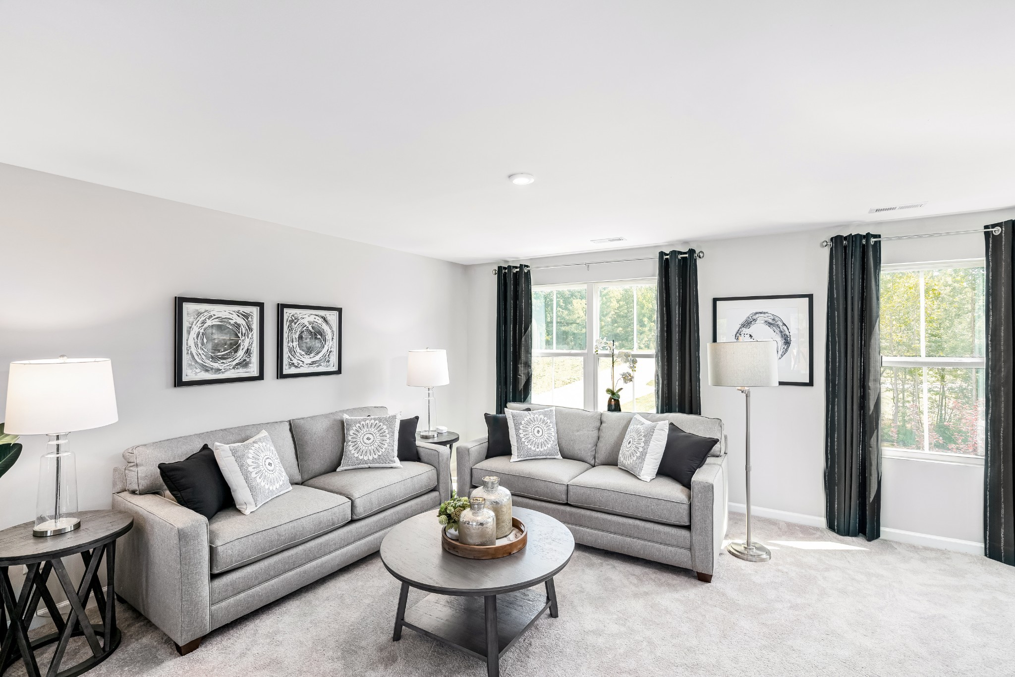 Staged living room with two gray sofas and large windows framed by black curtains.