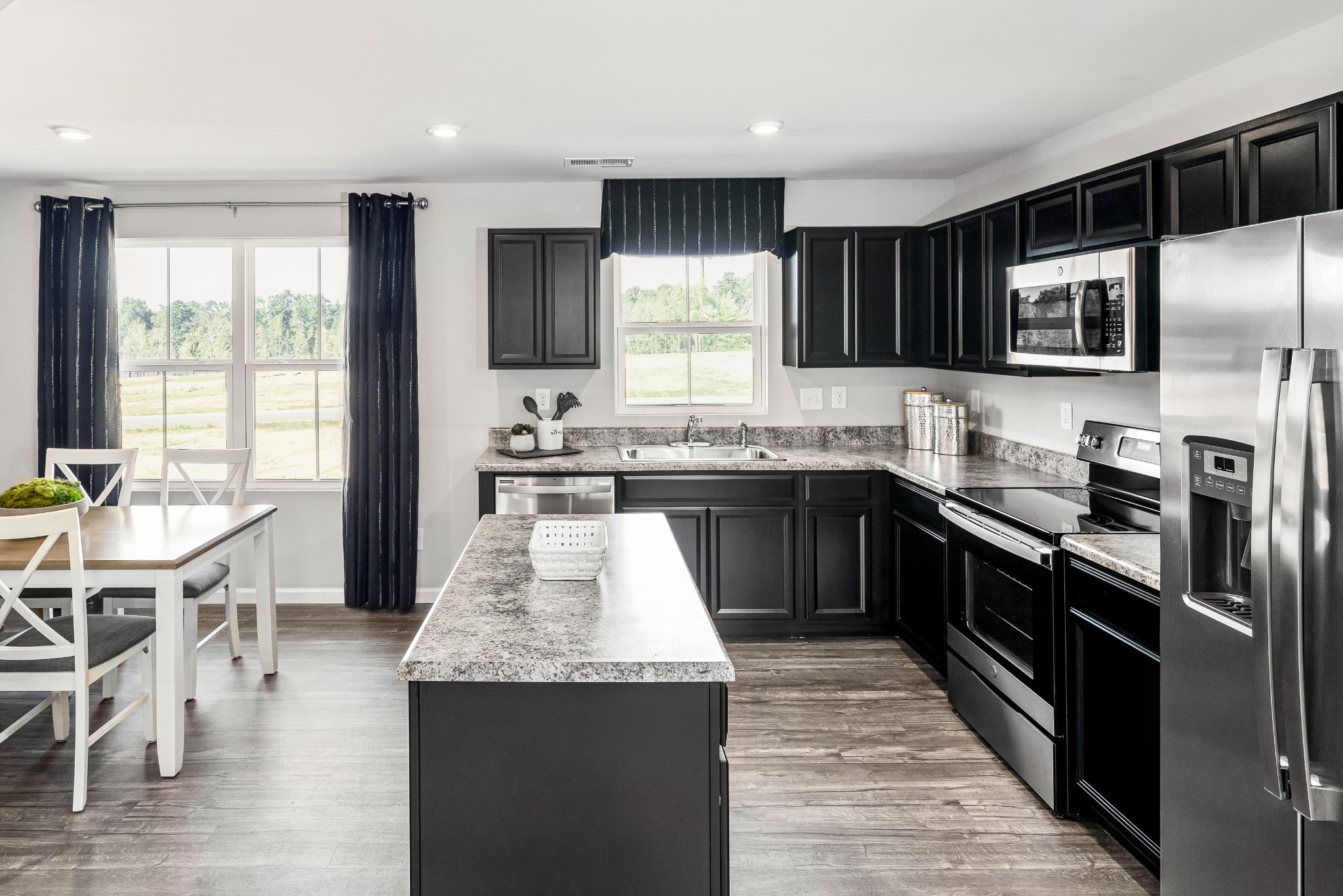 Kitchen with a large stone island, dark cabinets, stainless steel appliances, and adjoining dining area.