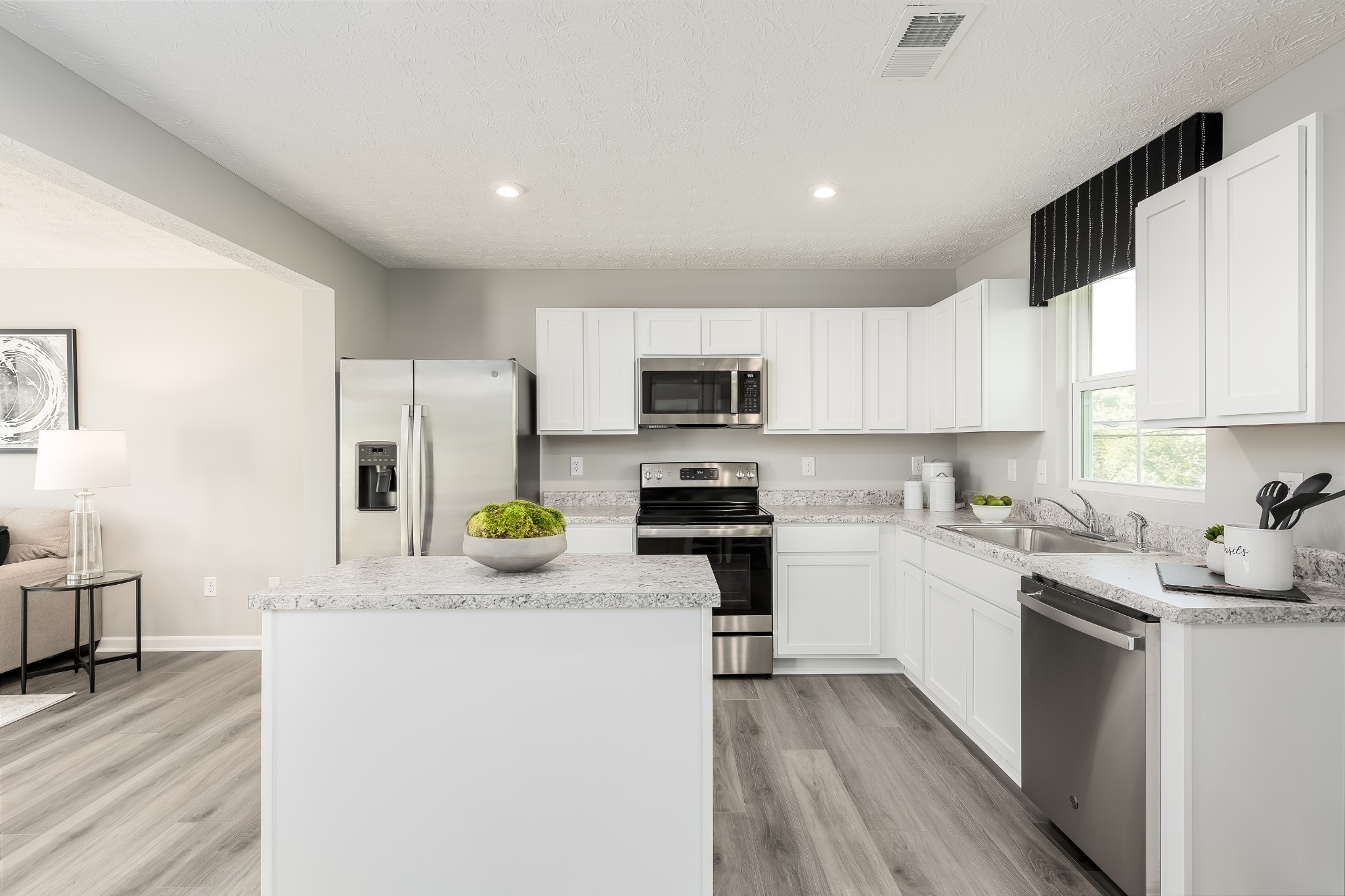 Bright kitchen with white cabinets, a large island, stainless appliances, and a sink beneath the window.