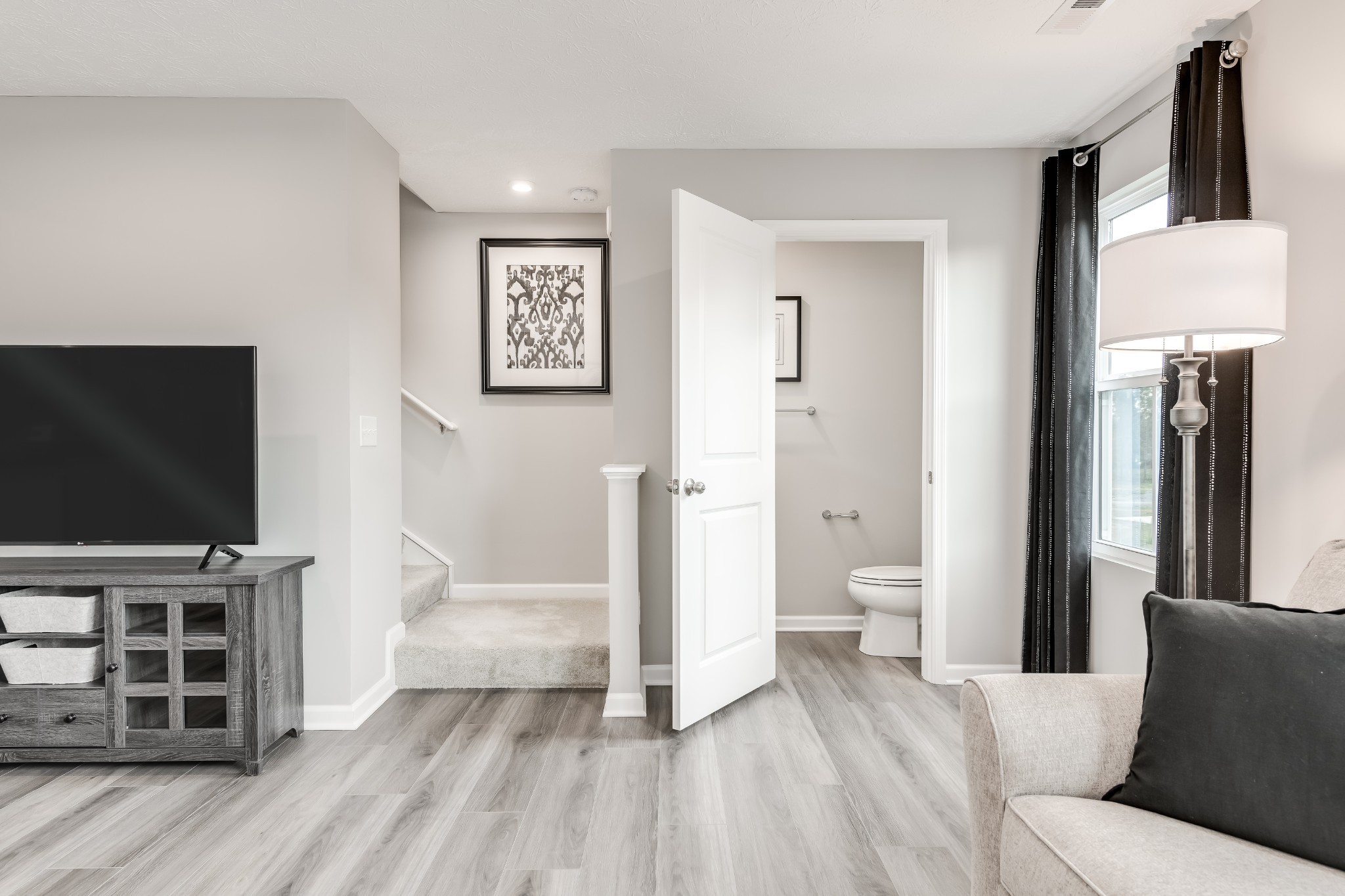 Furnished living room with a television, curtained window, and open doorway to a bathroom.