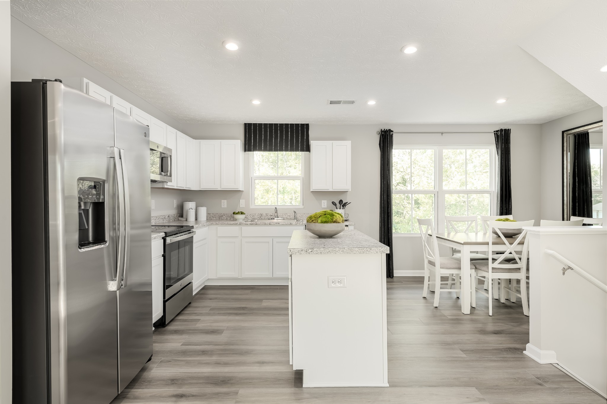 Kitchen and dining area with a central island, stainless steel appliances, and white dining set by large windows.