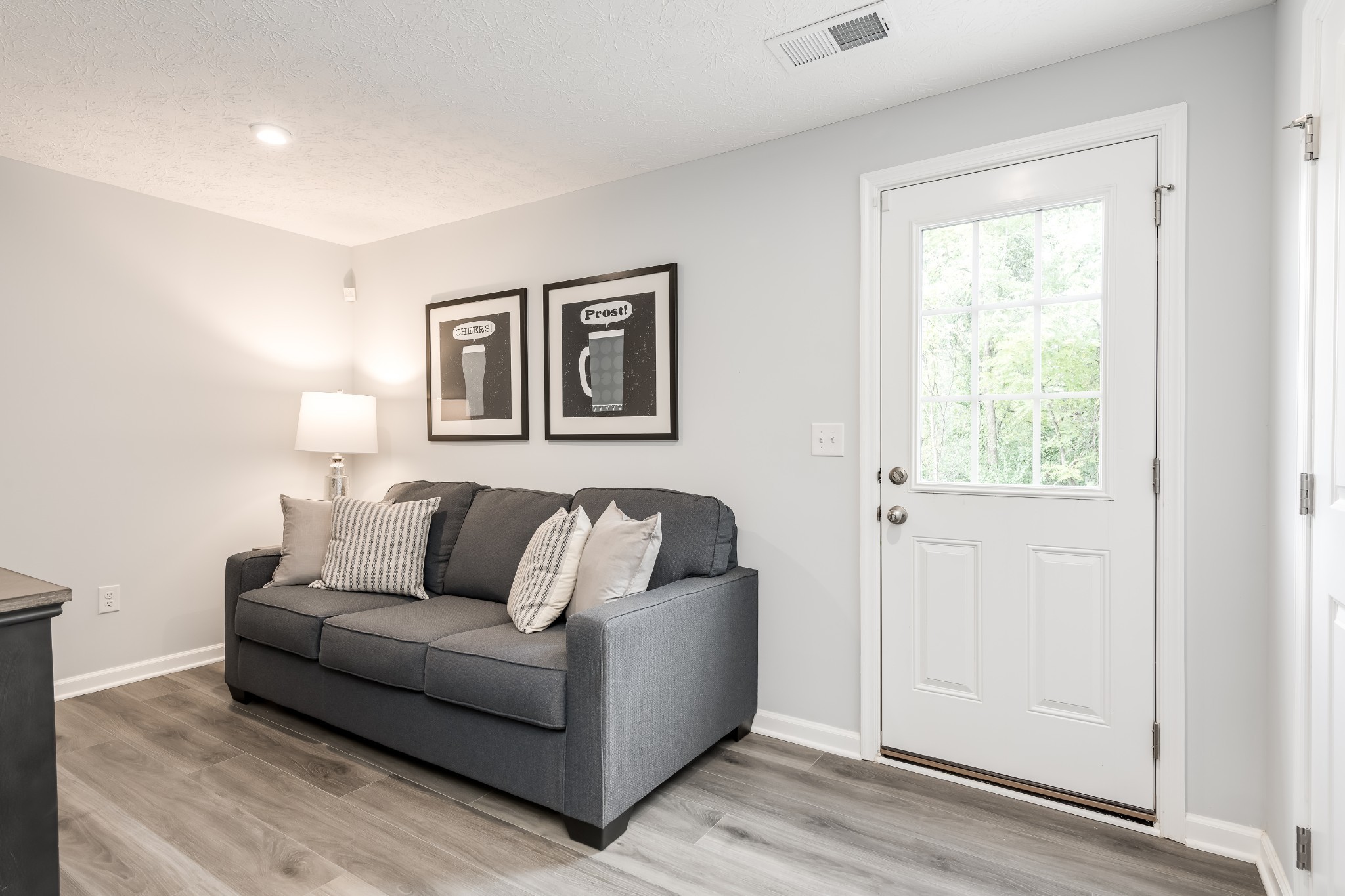 Living room with a gray sofa beside a white windowed door and framed beer-themed prints.