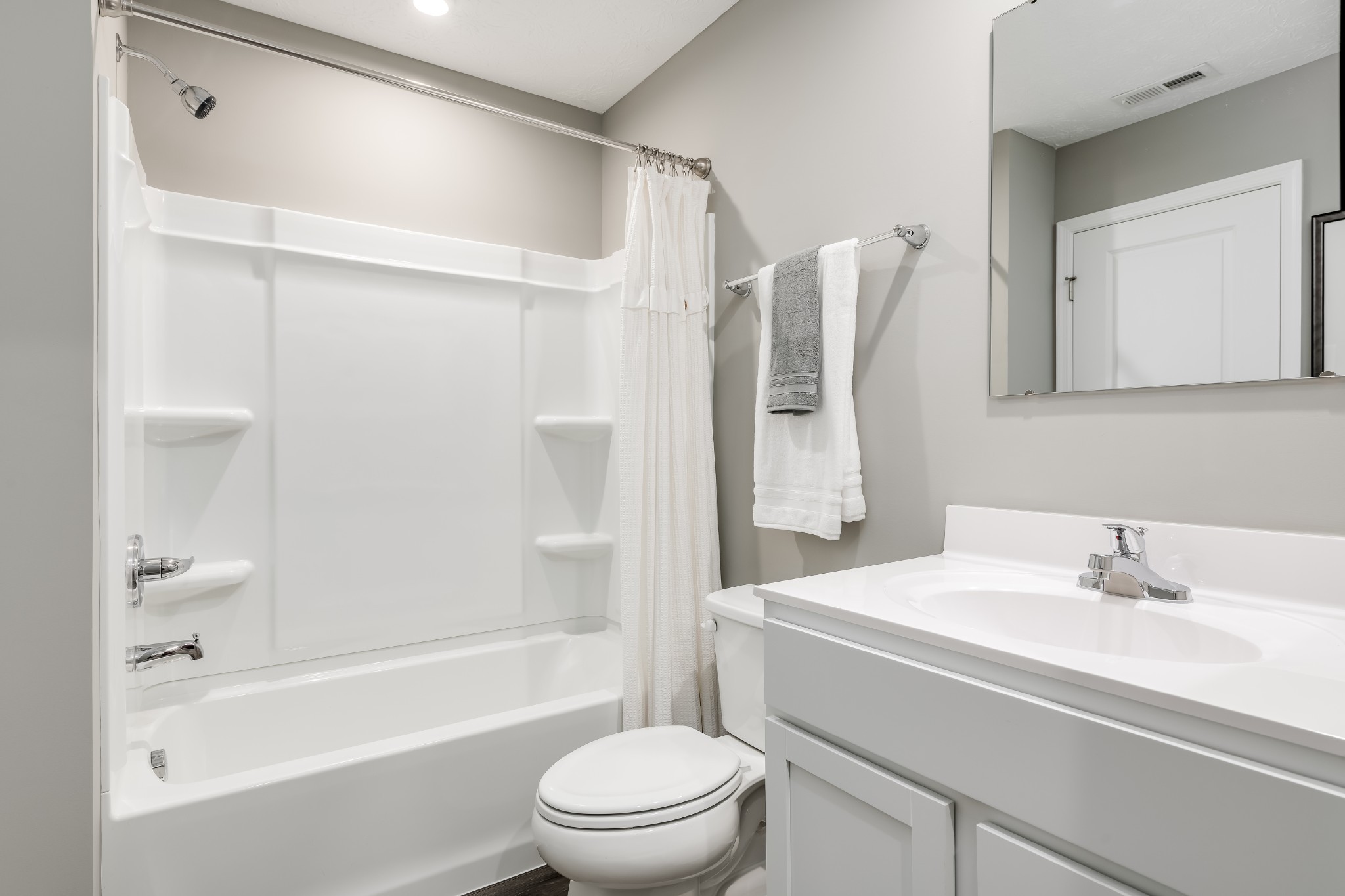 Bathroom with a white tub-shower, toilet, vanity, large mirror, and neatly hung towels.