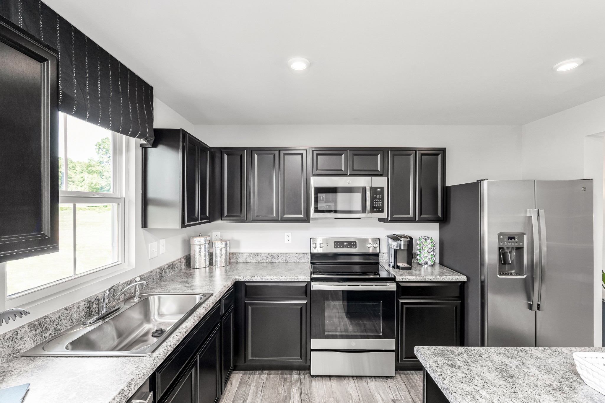 Kitchen with dark cabinets, stainless steel appliances, and a double-basin sink beneath a large window.