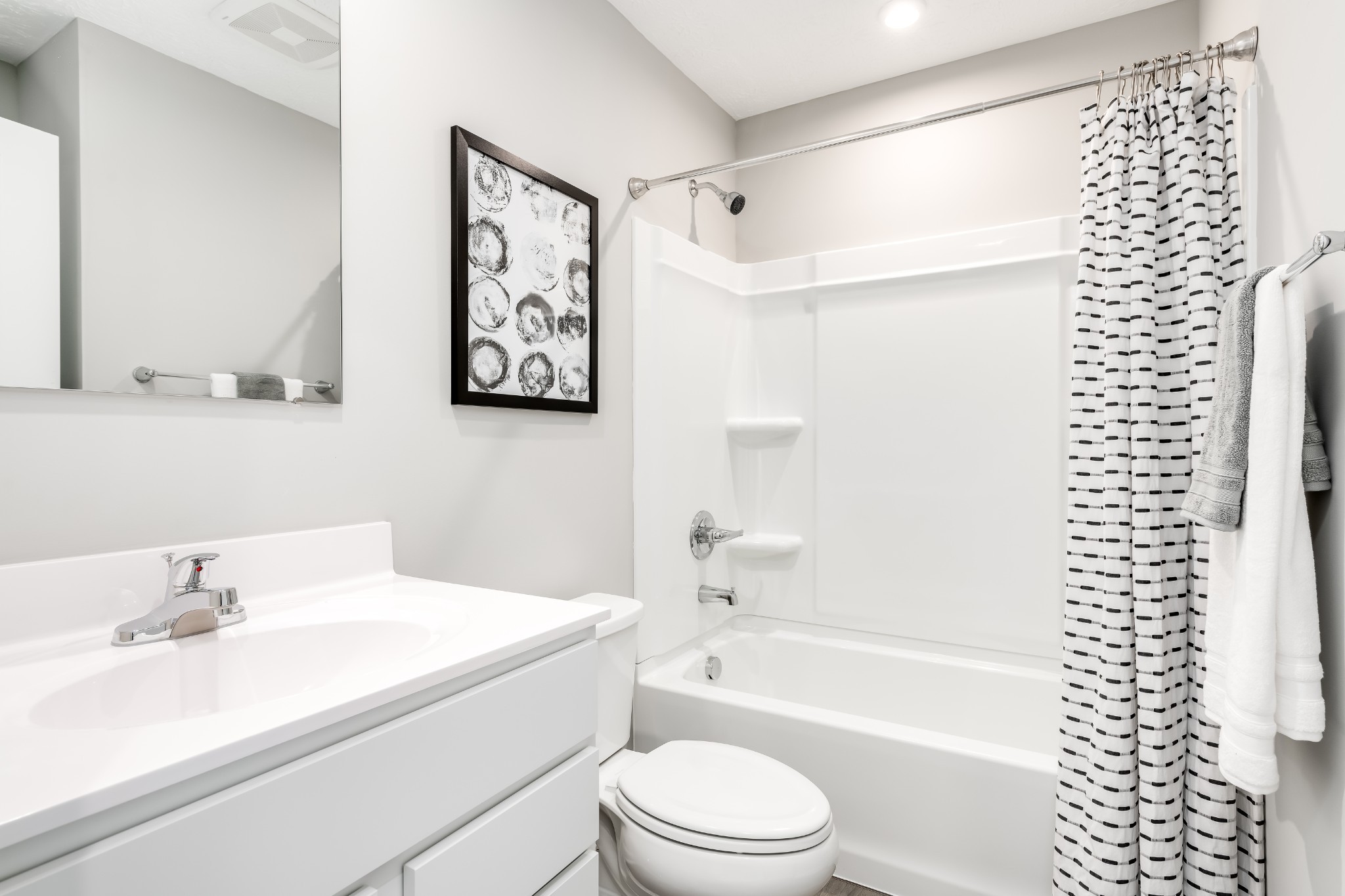 Bathroom with a white vanity, toilet, and tub behind a black-and-white patterned shower curtain.
