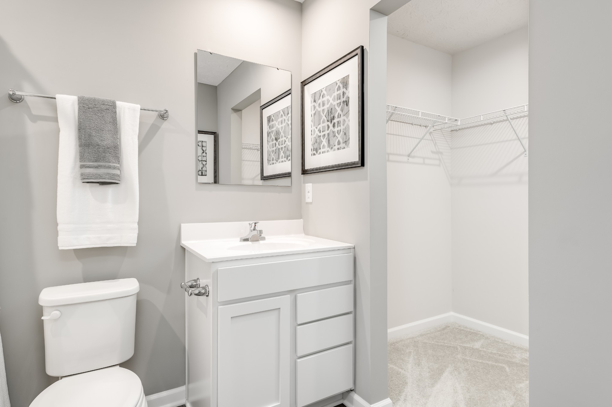 Bathroom with white vanity, toilet, gray and white towels, and an open carpeted closet.