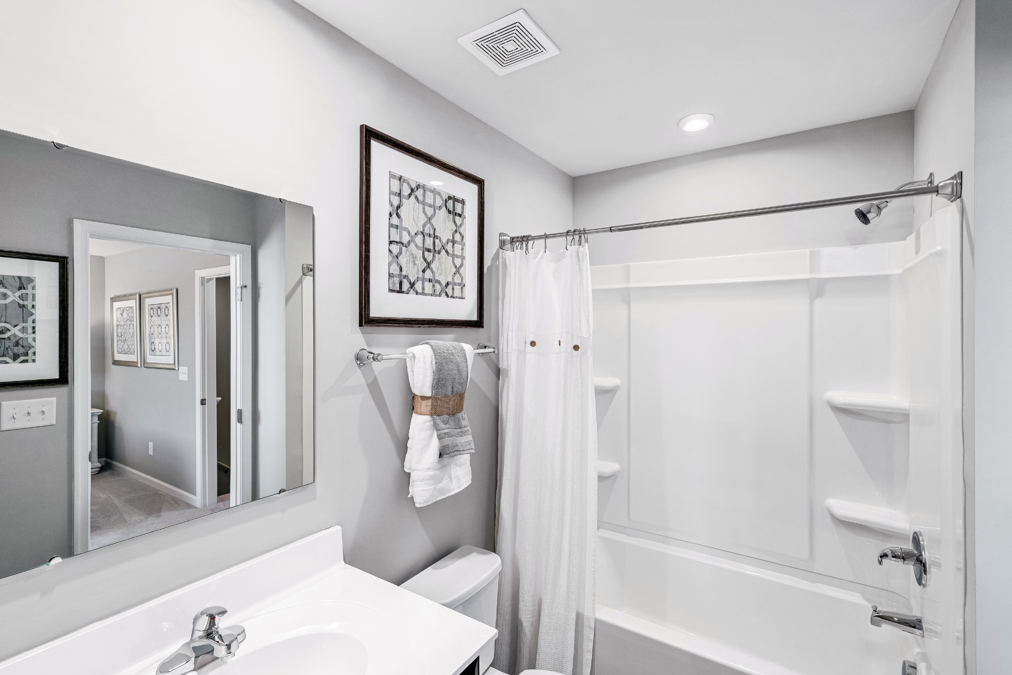 Bathroom with a white tub and shower, wide mirror, and towel-draped vanity wall.