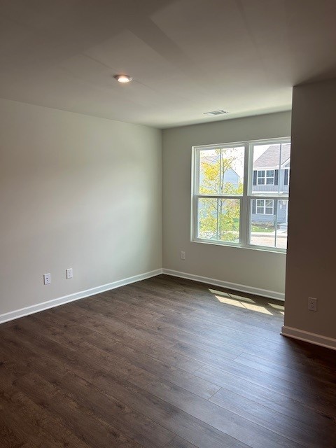 Empty room with dark wood-look flooring and a large window overlooking neighboring homes.